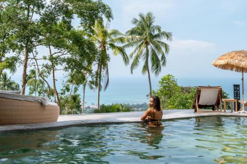 a woman sitting in a swimming pool at a resort at RoomQuest THEVA Resort Koh Samui in Koh Samui 