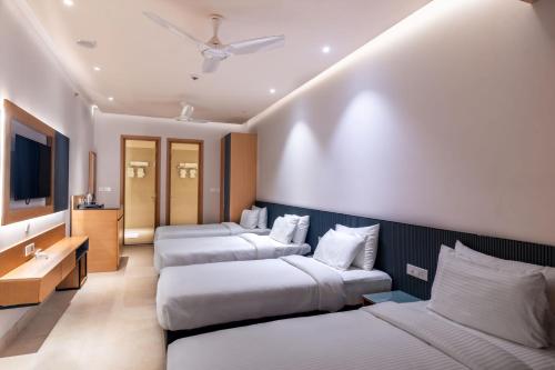a hotel room with three beds and a tv at Krishna's courtyard Hotel & Convention in Urāli