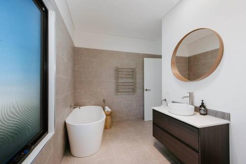a bathroom with a tub and a sink and a mirror at Frantoio Cottage - Serene Horizons, Stylish Comforts in McDonalds Creek