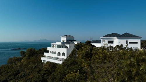 a white house on top of a hill next to the ocean at Miyue Shenzhen Blue and White Holy Island Cliff Pool Hotel in Shenzhen