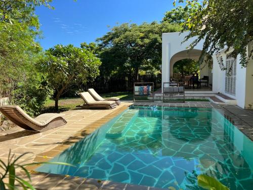 a swimming pool in a yard with chairs and a house at Villa Maridadi in Ukunda Airport