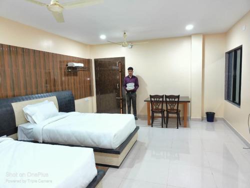 a man standing in a room with two beds and a table at whirlwind food court and resort in Numāligarh