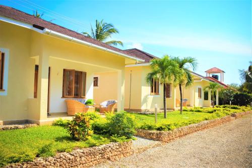 a yellow house with palm trees in the yard at V-Szameitat Homes in Diani Beach