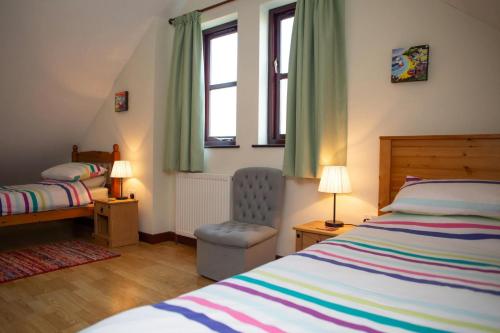 a bedroom with a bed and a chair and two windows at Tan-yr-Onnen Llangrannog in New Quay