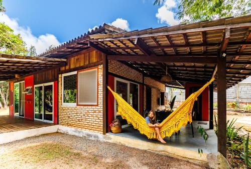 a woman sitting on a hammock outside of a house at Casa da Floresta Aruá, Praia do Forte, Bahia in Mata de Sao Joao