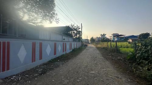 a dirt road next to a fence with the sun shining at Chitwan Comforts Apt 2 in Nārāyangarh