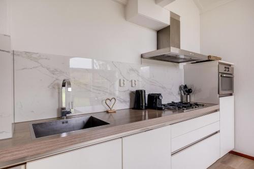 a white kitchen with a sink and a stove at Kruisbek I Chic Huisje met Riante Tuin in Zwiggelte