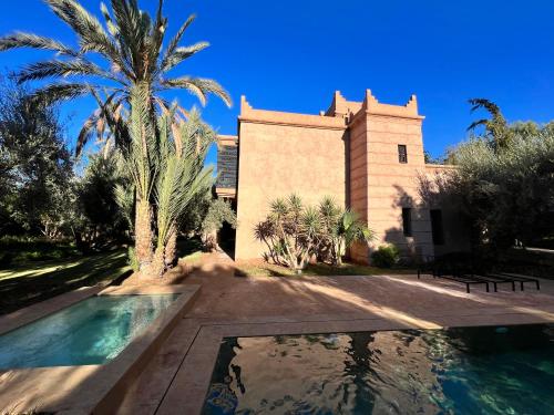 a building with a palm tree and a swimming pool at Villa kasbah de luxe, piscine et jacuzzi chauffés, jardin tropical in Marrakech
