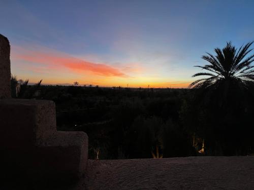 a sunset with a palm tree in the background at Villa kasbah de luxe, piscine et jacuzzi chauffés, jardin tropical in Marrakech
