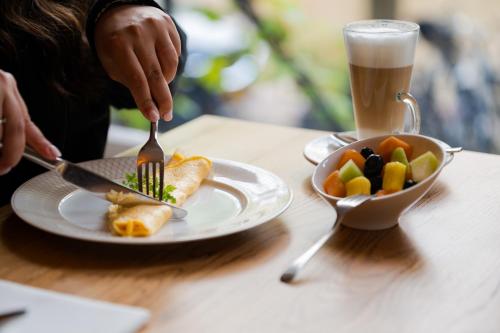 a person eating food on a plate with a fork and a bowl of fruit at Ambassade Hotel in Amsterdam