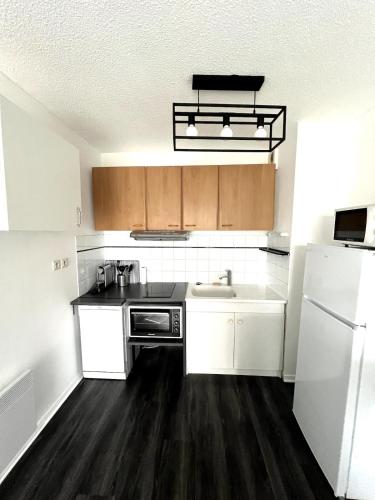 une cuisine avec des armoires blanches, un évier et un réfrigérateur dans l'établissement Aigues Marines - Appartement spacieux avec parking et terrasse, à Aytré