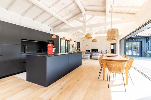 a kitchen and dining room with black cabinets and a table at Villa Agapi - 10 personnes, piscine chauffée, pétanque - Lège cap Ferret in Lège-Cap-Ferret