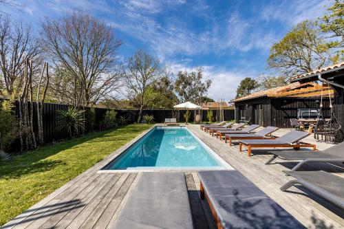 a swimming pool with lounge chairs and a house at Villa Agapi - 10 personnes, piscine chauffée, pétanque - Lège cap Ferret in Lège-Cap-Ferret