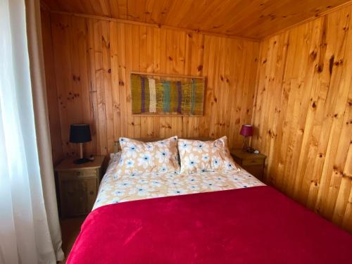 a bedroom with a red bed with wooden walls at Cabañas Refugio Las Conejas in Pelluhue