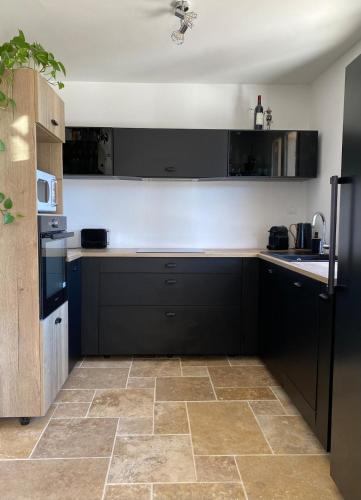 a kitchen with black cabinets and a tile floor at Maison proche centre village in Grignan