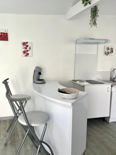 une cuisine blanche avec un comptoir et deux tabourets dans l'établissement Casa 4 Saisons - Studio à thème - PiscineJardin - Proche centre-ville, à Brive-la-Gaillarde