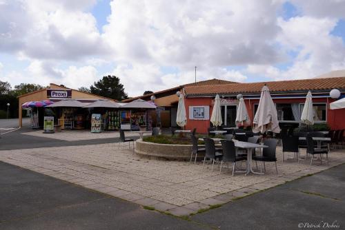a group of tables and chairs with umbrellas outside a building at Mobil-home 40m2, camping les Charmettes 4 étoiles La Palmyre 4-6 personnes-2 chambres dont 1 suite parentale-2 salles de bain in Les Mathes