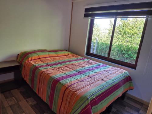 a bedroom with a bed with a colorful comforter and a window at Cabaña Araucaria in Chillán