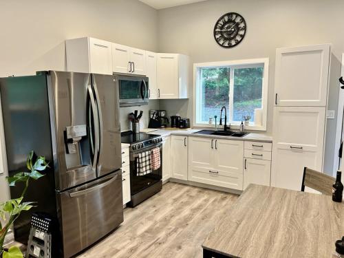 a kitchen with white cabinets and a stainless steel refrigerator at The Cottage - A Private Oceanfront Dream! in East Sooke