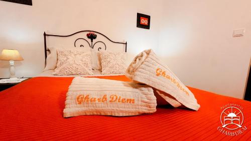 a bed with an orange blanket and pillows on it at Apartamentos Gharb Diem in Tavira