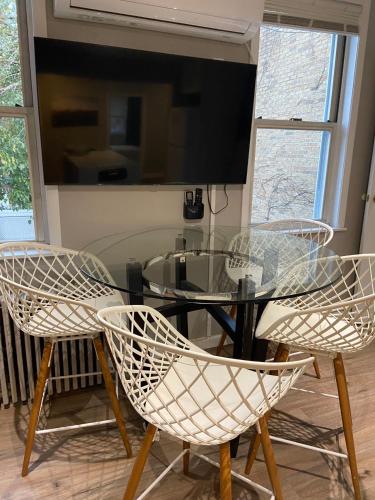 a glass table with three chairs and a television at Cozy Apartments Woodside near Manhattan in Queens