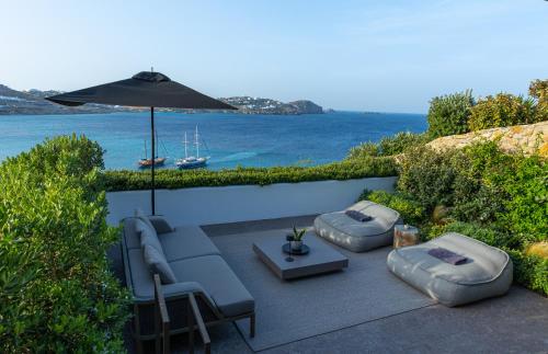 a patio with two chairs and an umbrella and the ocean at Noima Boutique Hotel Mykonos in Agios Ioannis Mykonos