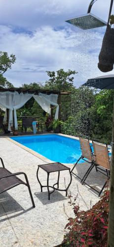 a swimming pool with two chairs and a table next to it at Chalé do João e do Chico Garfield in Jaboticatubas
