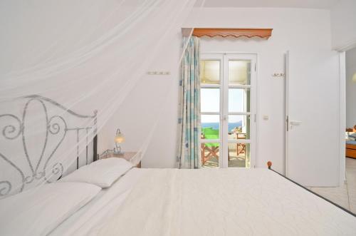a white bedroom with a large bed and a window at Ydreos Studios & Apartments in Mikri Vigla