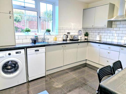 a kitchen with white cabinets and a washer and dryer at Cosy Luxurious Large 3 bedroom house, free parking, free WiFi in Havering atte Bower