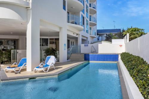 a swimming pool with two chairs and a building at Aqua Vista Resort in Maroochydore