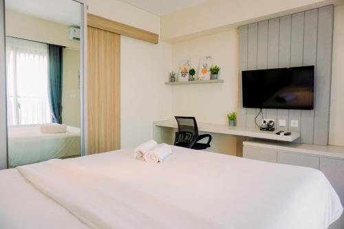 a bedroom with a large white bed and a tv at Homey and Simply Look 1BR Bintaro Embarcadero Apartment By Travelio in Tangerang