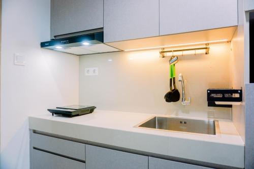 a white kitchen with a sink and a stove at Homey and Simply Look 1BR Bintaro Embarcadero Apartment By Travelio in Tangerang