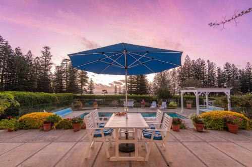 a patio with a table and a blue umbrella at Sunset Villa Norfolk Island - a Mediterranean inspired villa in Burnt Pine