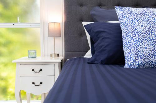 a bed with blue and white pillows and a night stand at Sunset Villa Norfolk Island - a Mediterranean inspired villa in Burnt Pine