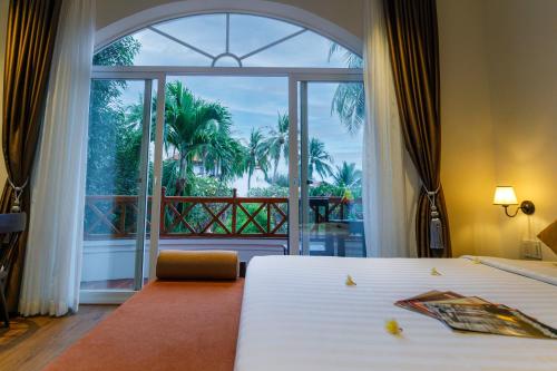 a bedroom with two beds and a large window at Le Aqua Resort & Spa Phan Thiet - Swiss Village Resort & Spa in Mui Ne