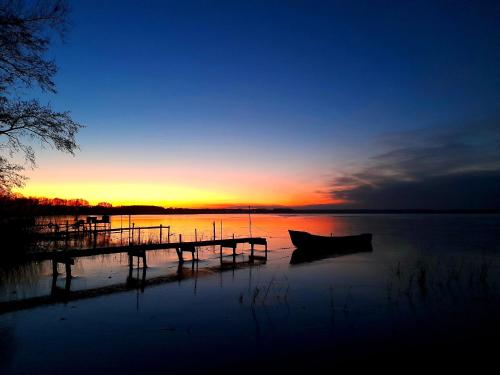 a dock with a boat on the water at sunset at Hausboot Am See Robert Döring in Riether Stiege