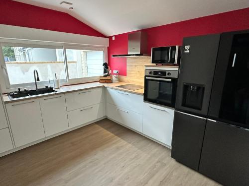 a kitchen with white cabinets and a red wall at Agréable maison neuve de plain pied in Villiers-le-Sec