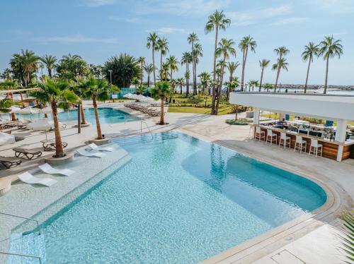 a pool at a resort with chairs and palm trees at Lordos Beach Hotel & Spa in Larnaka