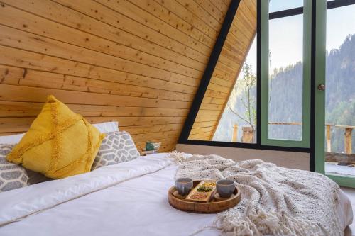 a bed with a tray of food and two cups on it at Vibrant A-Frame In The Valley By Bastiat Stays in Mandi