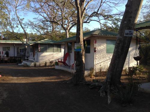 a white house with a red chair and trees at Hostal Villas Mexico in San Juan del Sur