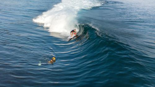 two people riding a wave on a surfboard in the ocean at Villa Searra - Ocean Breeze Boutique Hotel Hideaway Rooms in Canggu