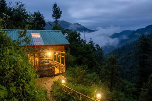 a cabin in the mountains at night with lights at Enchanting Cottage With Valley View By Bastiat Stays in Mandi