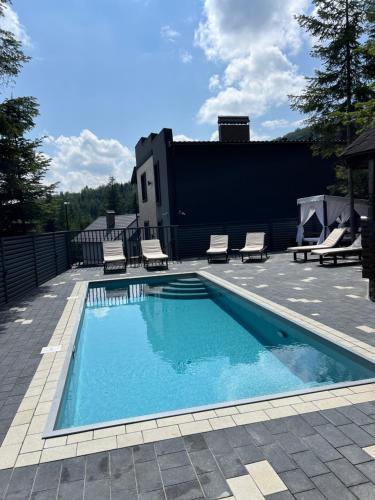 einem Pool mit zwei Liegestühlen und einem Gebäude in der Unterkunft VIP HOUSES Карпати Мигово in Myhowe