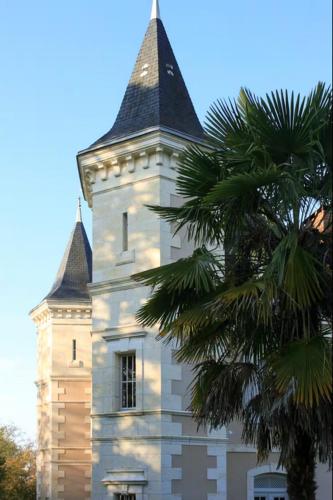 un grand bâtiment blanc avec une tour arborée dans l'établissement Le Château de Monciaux, à Bourrou