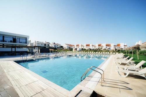 a large swimming pool with lounge chairs in a resort at Porto Covo Praia Hotel & SPA in Porto Covo