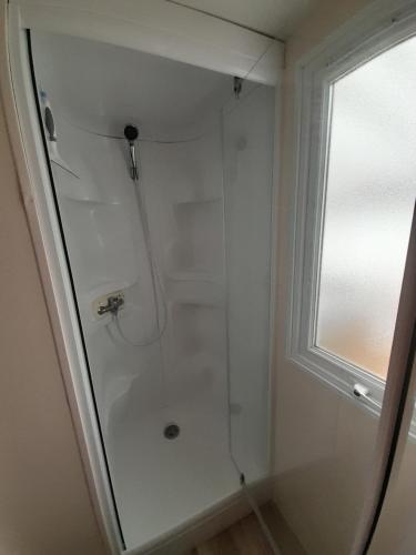 a shower with a glass door next to a window at Mobil home camping les Charmettes 4 étoiles les MATHES en Charente Maritime prés du ZOO de la Palmyre 8 personnes tout confort 3 chambres 2salles de bains 2 WC Lave linge lave vaisselle Climatisation bien situé in Les Mathes
