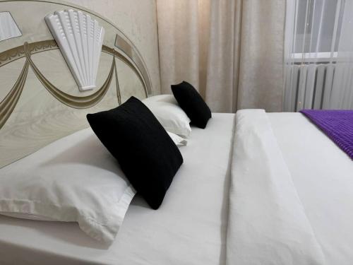 a white bed with black pillows on it at Апартаменты в центре города #2 in Aktobe