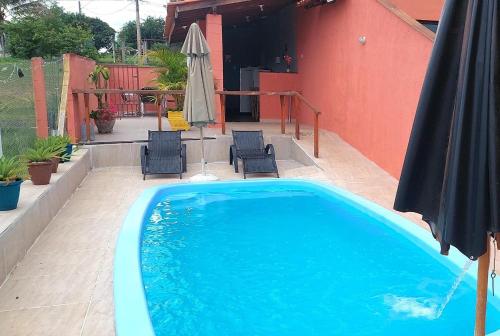 a blue swimming pool with chairs and an umbrella at Temporada Belas Casas in São Pedro