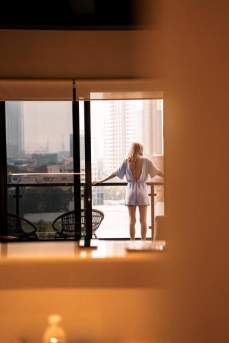 a woman standing on a balcony looking out of a window at VAUX Park Street Hotel - A collection of 8 luxury lofts in Colombo