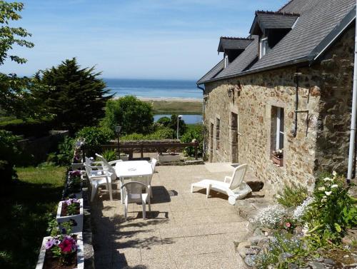 a patio with white chairs and tables and a building at Le Nid Vauville in Vauville